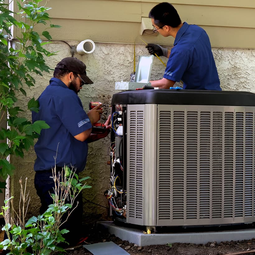 Two Hurley and David HVAC technicians installing a brand-new residential outdoor air conditioning condenser unit during a home AC replacement service.
