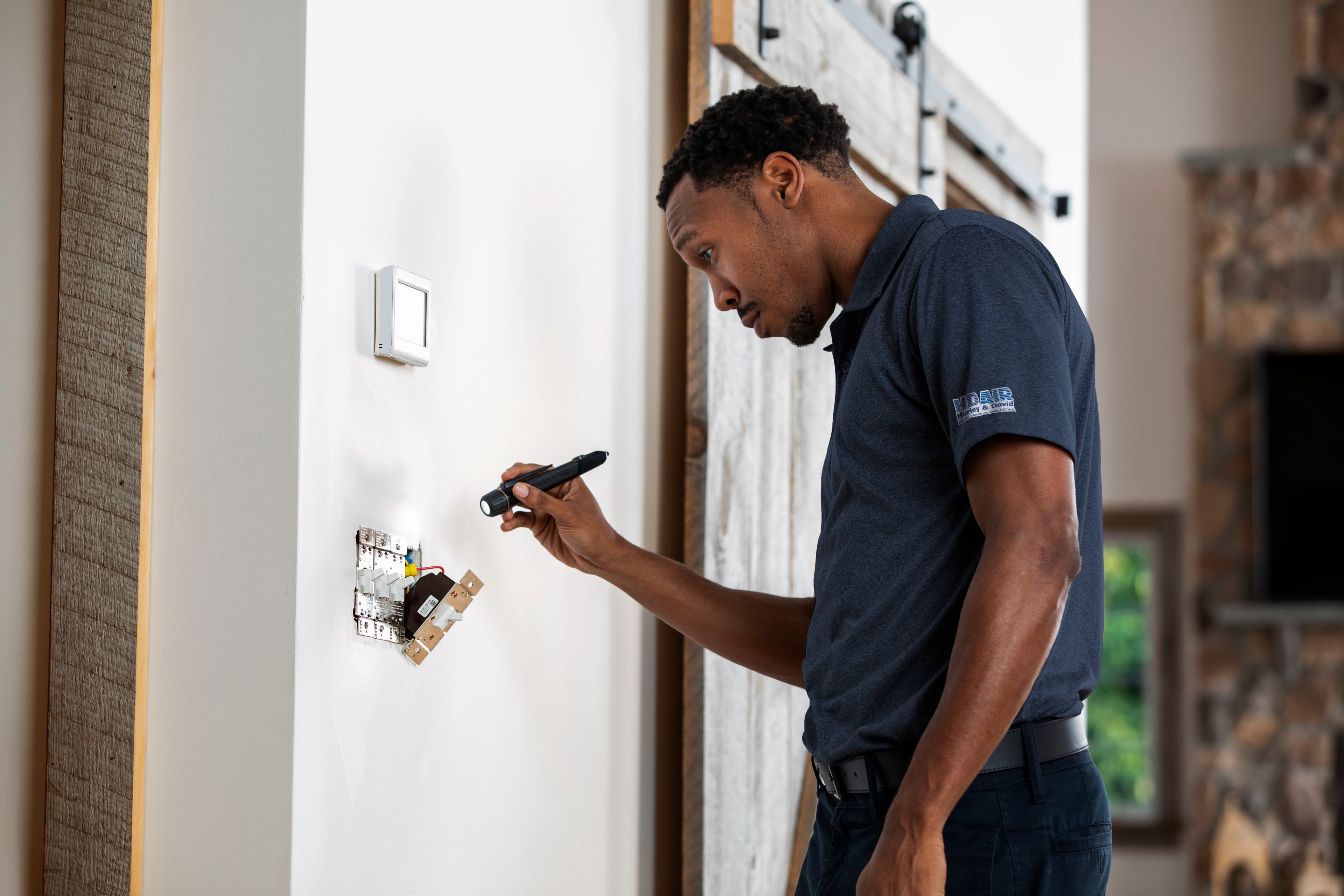 A professional Hurley and David electrician using a flashlight to safely inspect and troubleshoot exposed residential wall switch wiring during an electrical repair service.