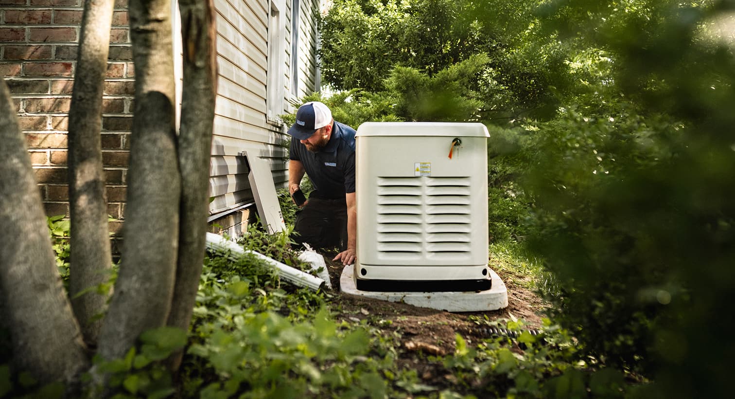 A professional Hurley and David technician inspects a large, beige whole-home standby generator installed on a concrete pad outside a residential house.