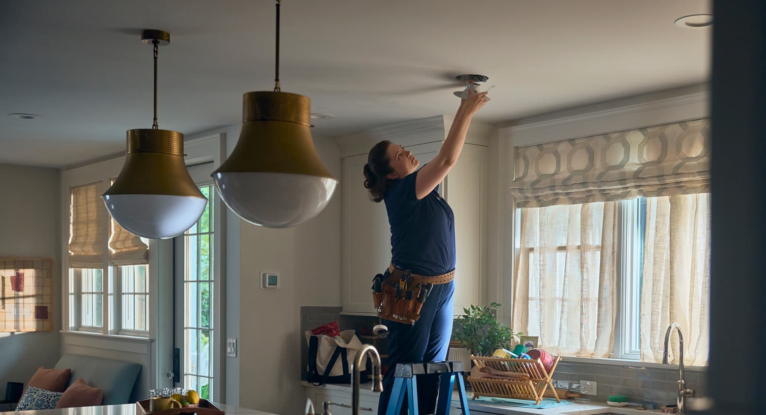 A professional Hurley and David electrician standing on a ladder to install modern recessed ceiling lights during a residential electrical installation service.
