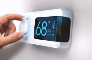 Hand turning a smart thermostat knob to set temperature on energy saving mode. fahrenheit units. Composite image between a photography and a 3D background.