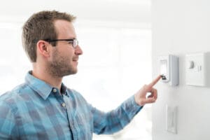 man setting his thermostat before leaving his house in winter
